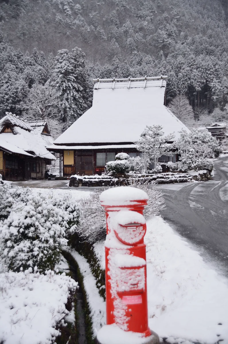 投稿写真：雪の中の茅葺屋根民家と赤い郵便ポスト